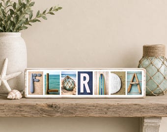Puede incluir: Un letrero rectangular de madera con la palabra FLORIDA deletreada en siete paneles fotográficos cuadrados individuales. Cada letra está representada por imágenes costeras que incluyen piedras, agua de mar, una boya de vidrio y madera.