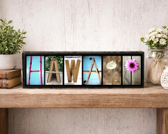 May include: A rectangular black frame containing six individual square photographs that spell out the word HAWAII. The images feature natural and structural elements shaped like letters, including a pink ladder, books, wood, and flowers.