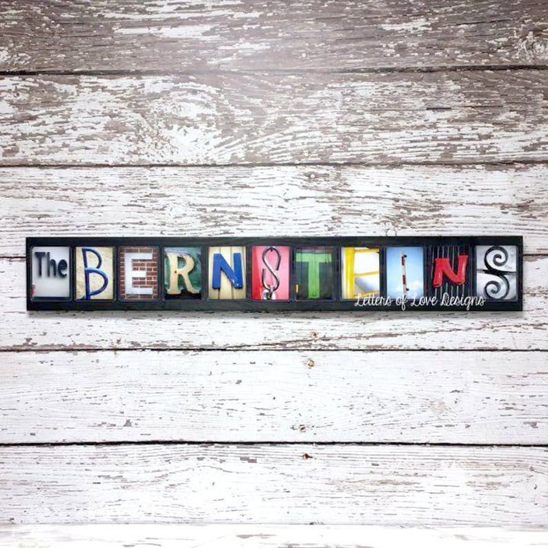 Puede incluir: Un letrero enmarcado en negro con el nombre "The Bernsteins" escrito en coloridas baldosas de letras individuales. Las letras tienen varios dise&ntilde;os y colores, incluyendo azul, rojo y ladrillo. El letrero est&aacute; sobre un fondo de madera blanca desgastada.