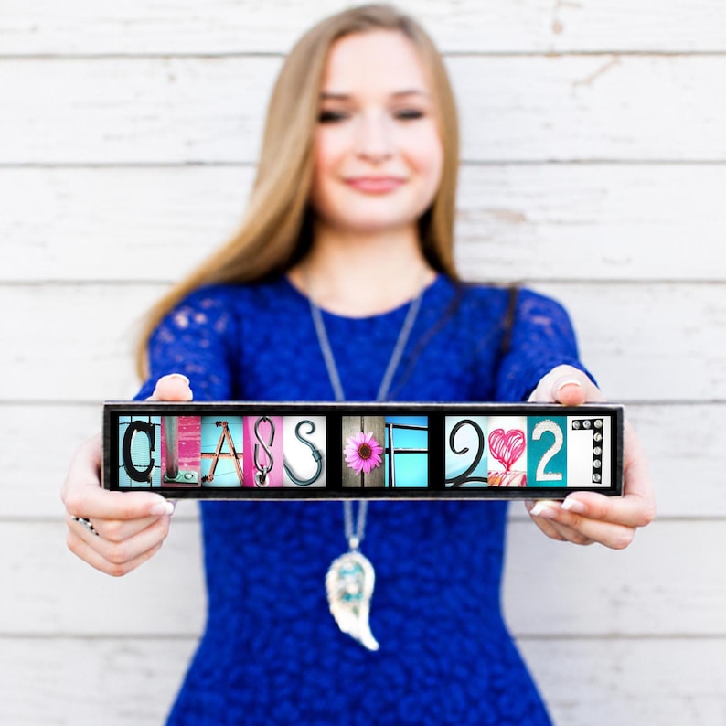 Puede incluir: Un letrero rectangular con el texto CLASS OF 2027, donde cada letra y n&uacute;mero est&aacute; representado por una imagen fotogr&aacute;fica &uacute;nica. Las letras se muestran en un marco negro, exhibiendo diversas texturas y colores, incluyendo una flor rosa.