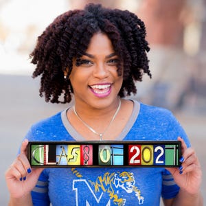 Puede incluir: Un letrero rectangular con marco negro que muestra el texto CLASS OF 2021, donde cada letra y n&uacute;mero est&aacute; representado por una imagen fotogr&aacute;fica &uacute;nica de un objeto con forma de car&aacute;cter, sobre un fondo vibrante y multicolor.
