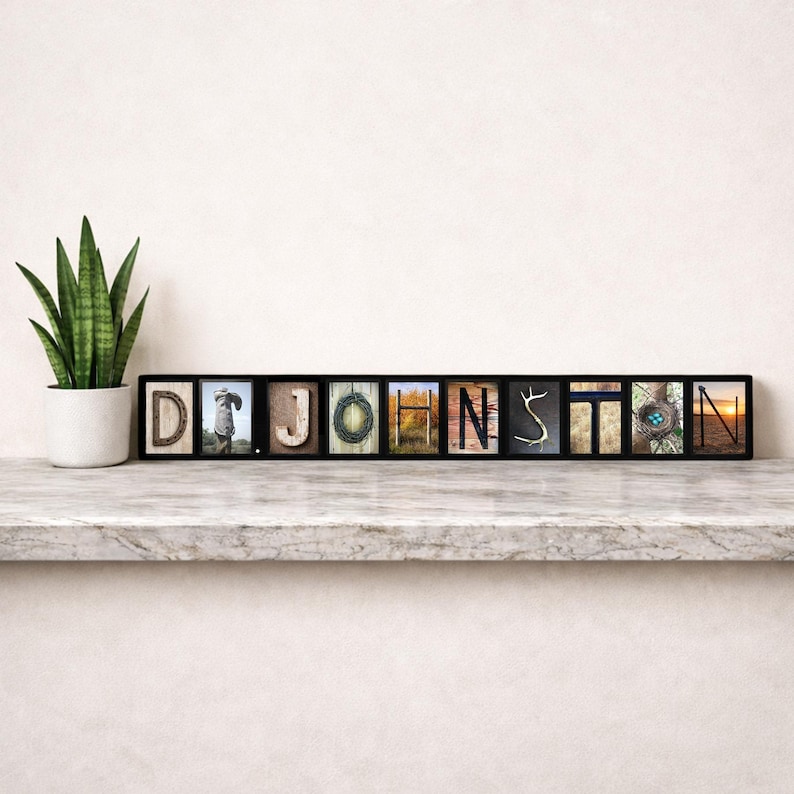 Puede incluir: Una pieza de arte mural enmarcada en negro que deletrea el nombre "JOHNSTON" con bloques de letras individuales. Cada bloque presenta una imagen &uacute;nica, incluyendo una persona, una corona y una puesta de sol. Una planta en maceta se encuentra a la izquierda.