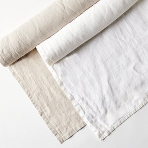 May include: Two rolls of fabric, one white and one beige, are laid out on a white surface. The fabric is folded and rolled up.