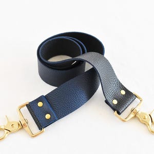 May include: A dark blue leather strap with gold hardware and two swivel clasps. The strap is approximately 1.5 inches wide.