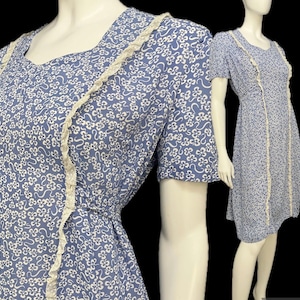 May include: A light blue dress with a white floral pattern and short sleeves. The dress features a square neckline and is trimmed with white lace along the edges and down the front. The dress is displayed on a mannequin.