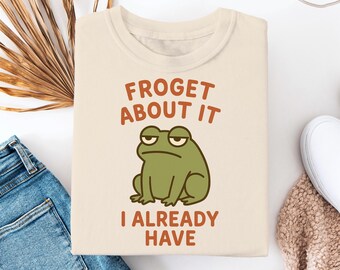 May include: A beige t-shirt with a green frog illustration and the text "Froget about it I already have".