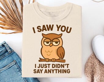 Puede incluir: Una camiseta beige con un gráfico de búho marrón y el texto "I saw you I just didn't say anything".