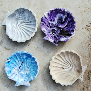 Peut inclure: Quatre plats décoratifs en forme de coquille avec des motifs marbrés. Les plats sont dans des tons de blanc, gris, violet et bleu.
