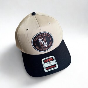 May include: A tan and black baseball cap with the text "TAILGATE'S & TOUCHDOWNS" on a circular patch. The cap has a black brim and a "OTTO" tag. The hat is a mid-profile, classic fit.