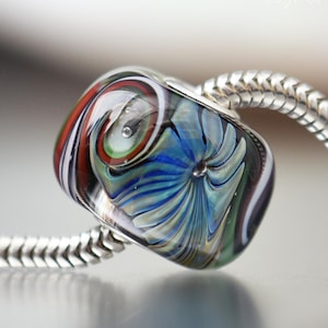 May include: A colorful glass bead with a blue, white, green, red, and black swirl pattern. The bead is on a silver chain.