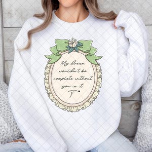 Puede incluir: Sudadera blanca con un dise&ntilde;o ovalado, un lazo verde y el texto "My dream wouldn't be complete without you in it." El dise&ntilde;o incluye un acento floral y una "T" estilizada.