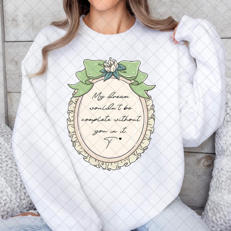 Puede incluir: Sudadera blanca con un dise&ntilde;o ovalado, un lazo verde y el texto "My dream wouldn't be complete without you in it." El dise&ntilde;o incluye un acento floral y una "T" estilizada.