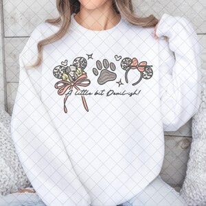 May include: White sweatshirt with a graphic design featuring mouse ears, a paw print, and the text "A little bit Devil-ish!". The design includes a bow and star accents. The sweatshirt is a casual, everyday wear item.