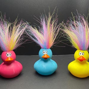 May include: Three rubber duck toys with colorful, spiky hair. The ducks are pink, blue, and yellow.