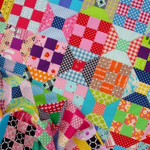 May include: A colourful patchwork quilt made of various fabrics with different patterns, including polka dots, stripes and checkered designs. The quilt is made up of squares and rectangles, and the colours are bright and vibrant.