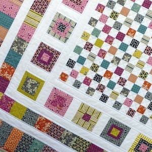 May include: A white quilt with a patchwork design featuring squares of various colors and patterns, including pink, yellow, green, blue, and orange. The quilt is made up of smaller squares sewn together to create a larger design.