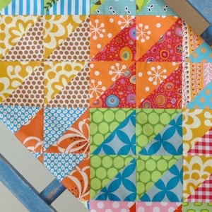 以下が含まれることがあります： 青、緑、オレンジ、ピンク、茶色、白の色合いで、さまざまな幾何学模様が施されたカラフルなパッチワークキルトです。