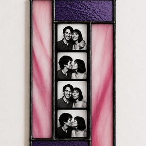 Peut inclure: Un cadre photo rectangulaire en vitrail avec une colonne verticale centrale de quatre photographies carrées en noir et blanc d'un couple. Le cadre est bordé de panneaux de verre violet texturé en haut et en bas et de panneaux roses.