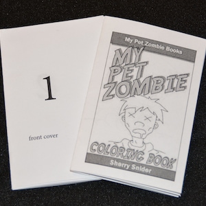 Può includere: Un libro da colorare in bianco e nero intitolato "My Pet Zombie Coloring Book" di Sherry Snider. La copertina presenta uno zombie dei cartoni animati con una macchia di bava e X per gli occhi.
