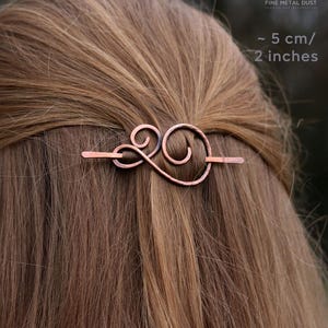 May include: A copper hair clip with a swirling design. The clip is about 5 cm or 2 inches long.