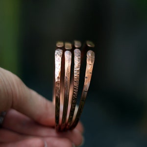 Op de afbeelding: Vier koperen armbanden gestapeld, elk met een gehammerde textuur.
