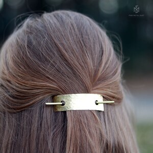 May include: A gold hammered metal bar hair clip with two small holes and a thin gold bar extending from each hole. The clip is in a person's hair.