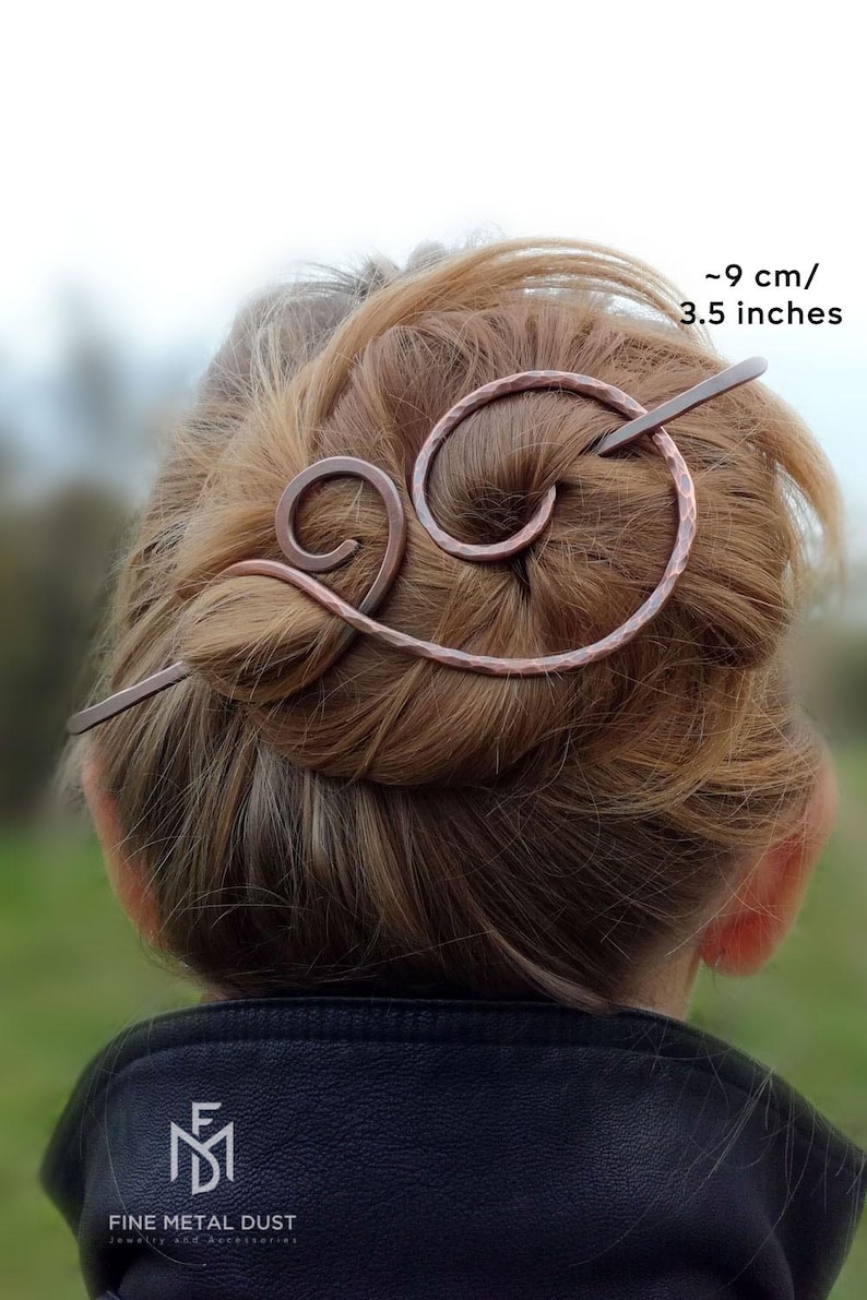 May include: A copper hair stick with a hammered finish and a double swirl design. The stick is 9 cm / 3.5 inches long.