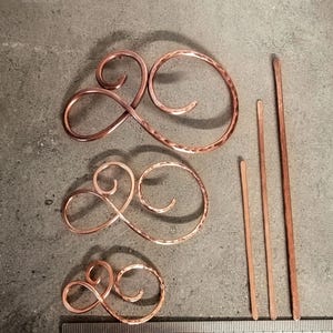 May include: Three copper hair pins, two are curly and one is straight. The curly hair pins are hammered and come in three sizes. The straight hair pin is 10 cm long.