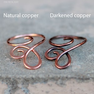May include: Two copper wire rings, one with a natural copper finish and the other with a darkened copper finish. The rings are shaped like a stylized infinity symbol.