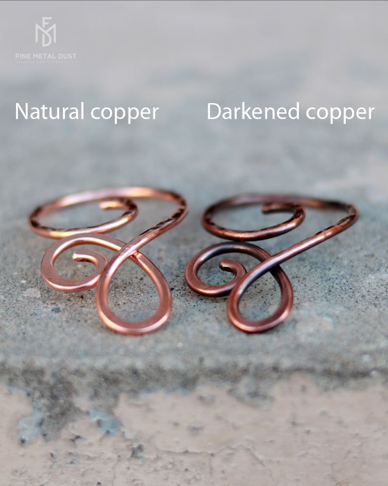 May include: Two copper wire rings, one with a natural copper finish and the other with a darkened copper finish. The rings are shaped like a stylized infinity symbol.