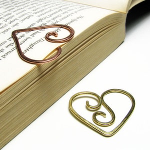 May include: Two heart-shaped bookmarks, one copper and one gold, with a swirl design. The copper bookmark is on top of a closed book.