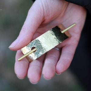 May include: A gold hammered metal hair stick with a smooth, round pin. The stick is rectangular and has a hammered texture.