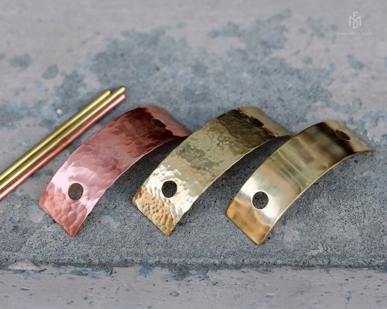 May include: Three metal strips in different finishes: copper, brass, and polished brass. Each strip is curved and has two holes. The strips are arranged in a row, with the copper strip on the left, the brass strip in the middle, and the polished brass strip on the right.