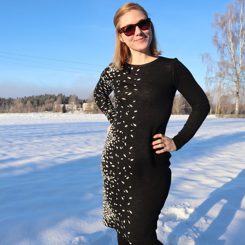Puede incluir: Un vestido negro de manga larga con un estampado abstracto blanco. El vestido es ajustado y tiene un escote redondo. La persona que lleva el vestido est&aacute; de pie en un campo nevado.
