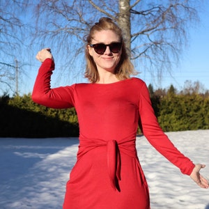 Puede incluir: Una mujer con un vestido rojo de manga larga con un lazo en la cintura. Lleva gafas de sol y tiene el pelo recogido hacia atr&aacute;s. El fondo es un paisaje nevado.