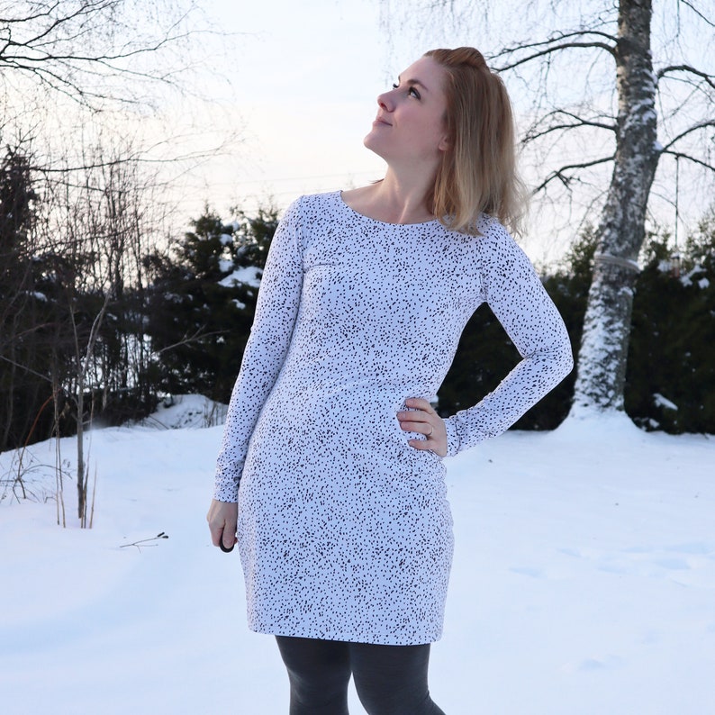 Puede incluir: Un vestido blanco con estampado de lunares negros. El vestido tiene mangas largas y un escote redondo. La persona que lleva el vestido est&aacute; de pie en un paisaje nevado.