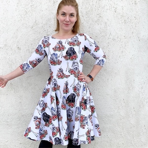 May include: A white dress with a floral print featuring Star Wars characters, including Darth Vader, R2-D2, and C-3PO. The dress has a fitted bodice and a flared skirt.