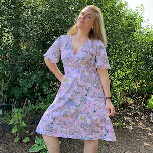 May include: A pink wrap dress with a floral and animal print. The dress has a V-neckline and short sleeves with ruffled edges. The dress is knee-length and has a flowy skirt.