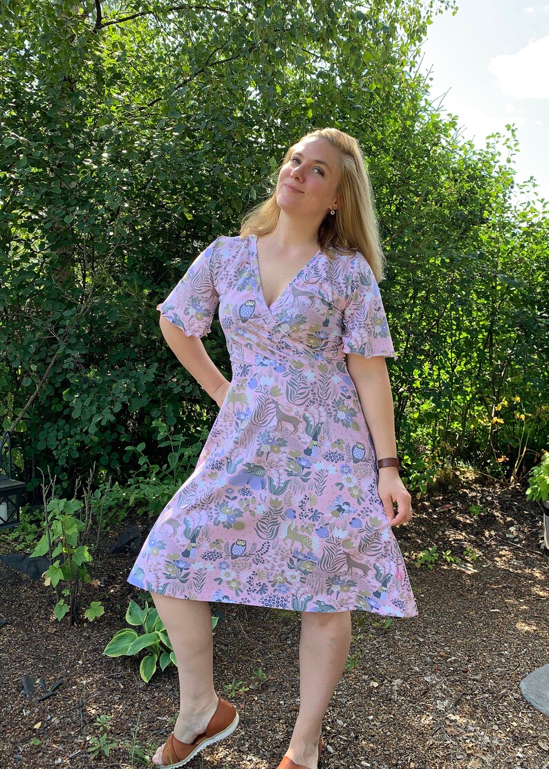 May include: A pink wrap dress with a floral and animal print. The dress has a V-neckline and short sleeves with ruffled edges. The dress is knee-length and has a flowy skirt.