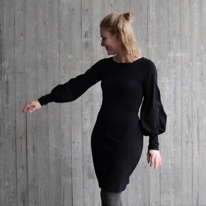 Puede incluir: Un vestido negro de manga larga con un corpi&ntilde;o ajustado y una falda ligeramente acampanada. El vestido tiene mangas grandes y abullonadas que se recogen en la mu&ntilde;eca.