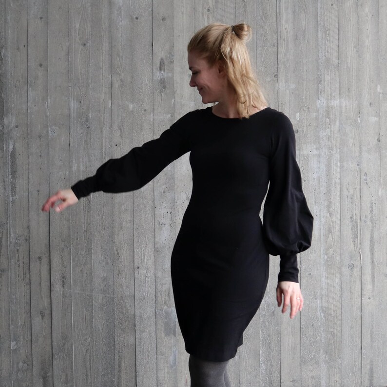 Puede incluir: Un vestido negro de manga larga con un corpi&ntilde;o ajustado y una falda ligeramente acampanada. El vestido tiene mangas grandes y abullonadas que se recogen en la mu&ntilde;eca.