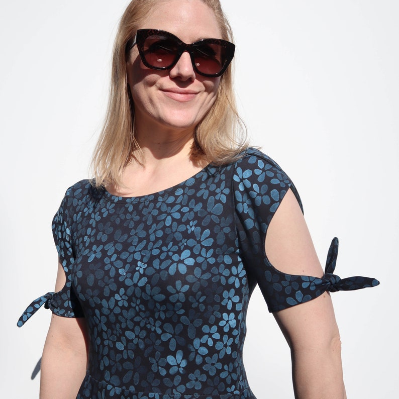 Puede incluir: Un vestido de estampado floral azul y negro con mangas cortas que se atan en la mu&ntilde;eca. El vestido tiene un escote redondo y un corte holgado.