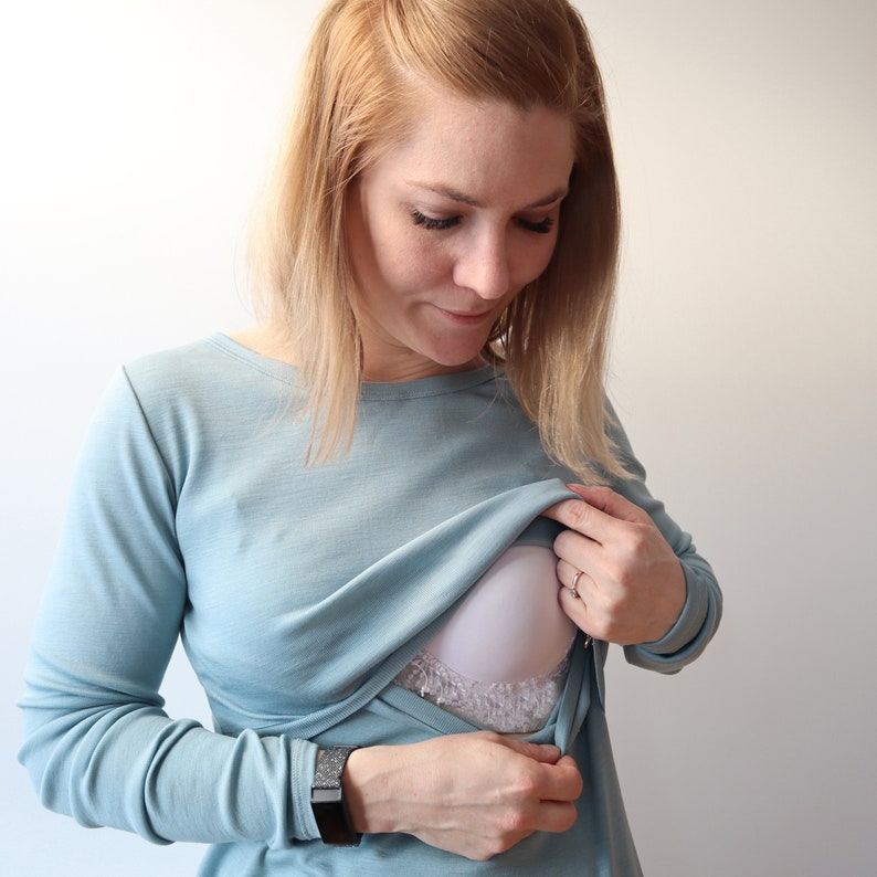 May include: A woman wearing a light blue long-sleeved shirt with a white nursing bra peeking out from the neckline.