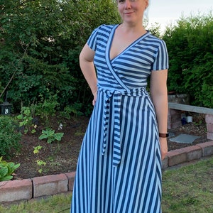 May include: A woman wearing a blue and white striped maxi dress with a wrap style bodice and a tie belt. The dress has short sleeves and a V-neckline.