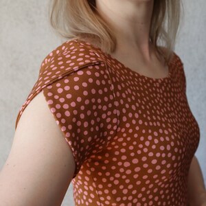 Puede incluir: Una camisa de manga corta con lunares marrones y rosas y cuello redondo.