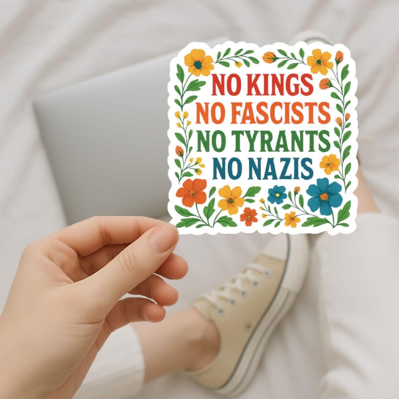 May include: A square sticker with the text "NO KINGS NO FASCISTS NO TYRANTS NO NAZIS" in red, orange, green, and blue. The text is surrounded by a floral border with orange, yellow, and blue flowers and green leaves.