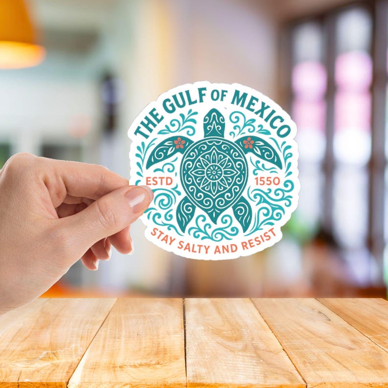 May include: A round sticker with a teal turtle design and the text "THE GULF OF MEXICO" and "ESTD 1550". The sticker also says "STAY SALTY AND RESIST" in red and white. The sticker is held by a hand.