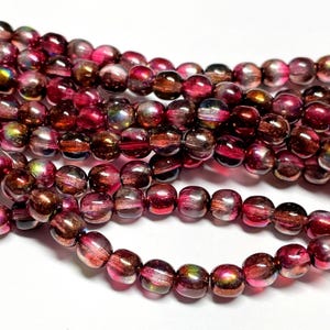 May include: Strands of iridescent glass beads in shades of red, pink, and brown. The round beads have a marbled appearance, with a mix of colors and a glossy finish. These beads are suitable for jewelry making.