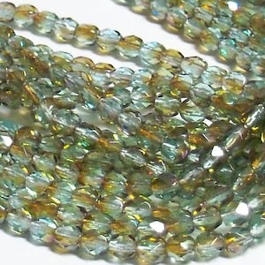 May include: A strand of iridescent green and gold glass beads. The beads are faceted and have a slightly irregular shape.