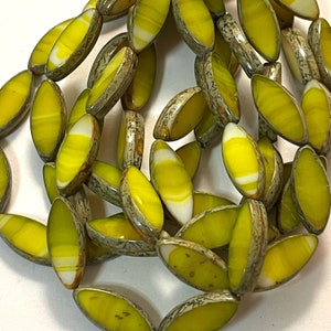 May include: A strand of yellow and white oval-shaped beads with a mottled gray and brown pattern. The beads are made of glass and have a glossy finish.